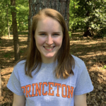 Photo depicts woman smiling at camera with light red hair, wearing a gray Princeton t-shirt and standing in front of a tree.