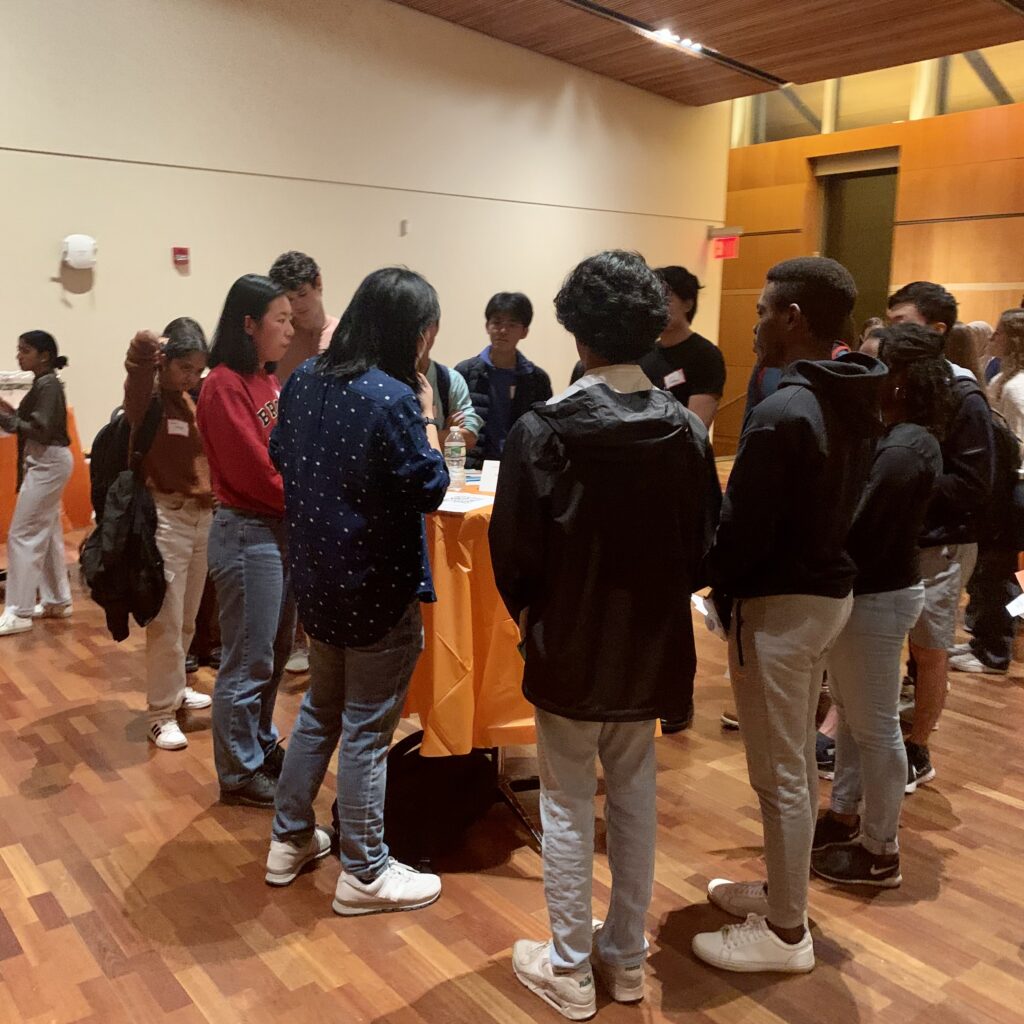 Photo of ReMatch table at the Carl A. Fields Center Multipurpose Room. Mentors and mentees are standing around a tall bistro table covered in an orange tablecloth. 