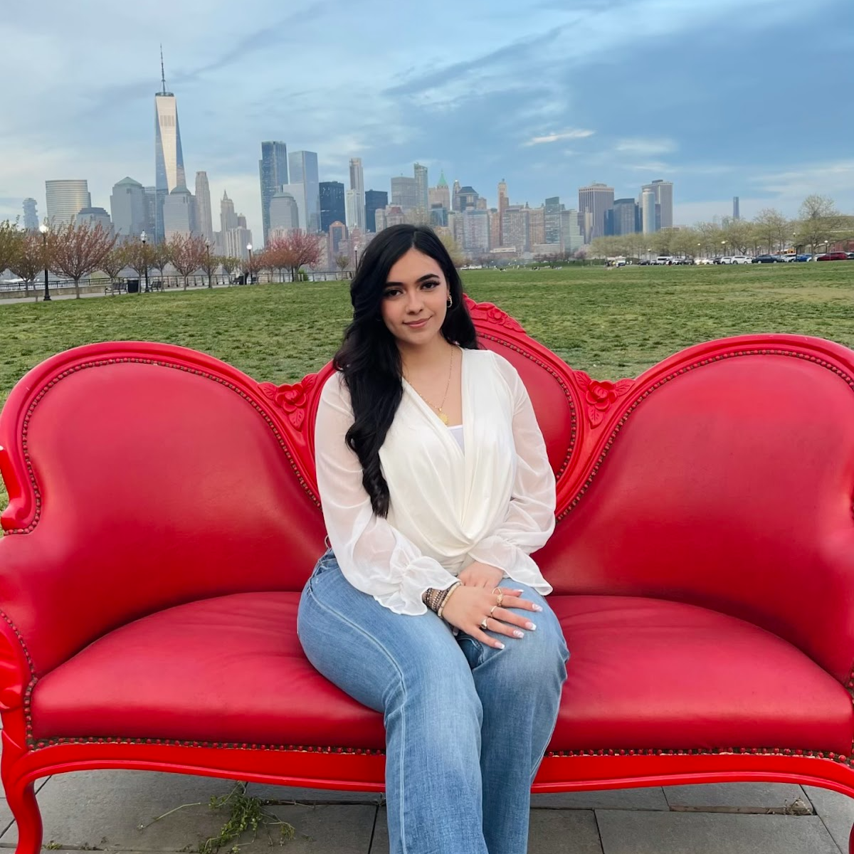Cara Khalifeh sitting on a red bench in central park with the NYC skyline in the background.