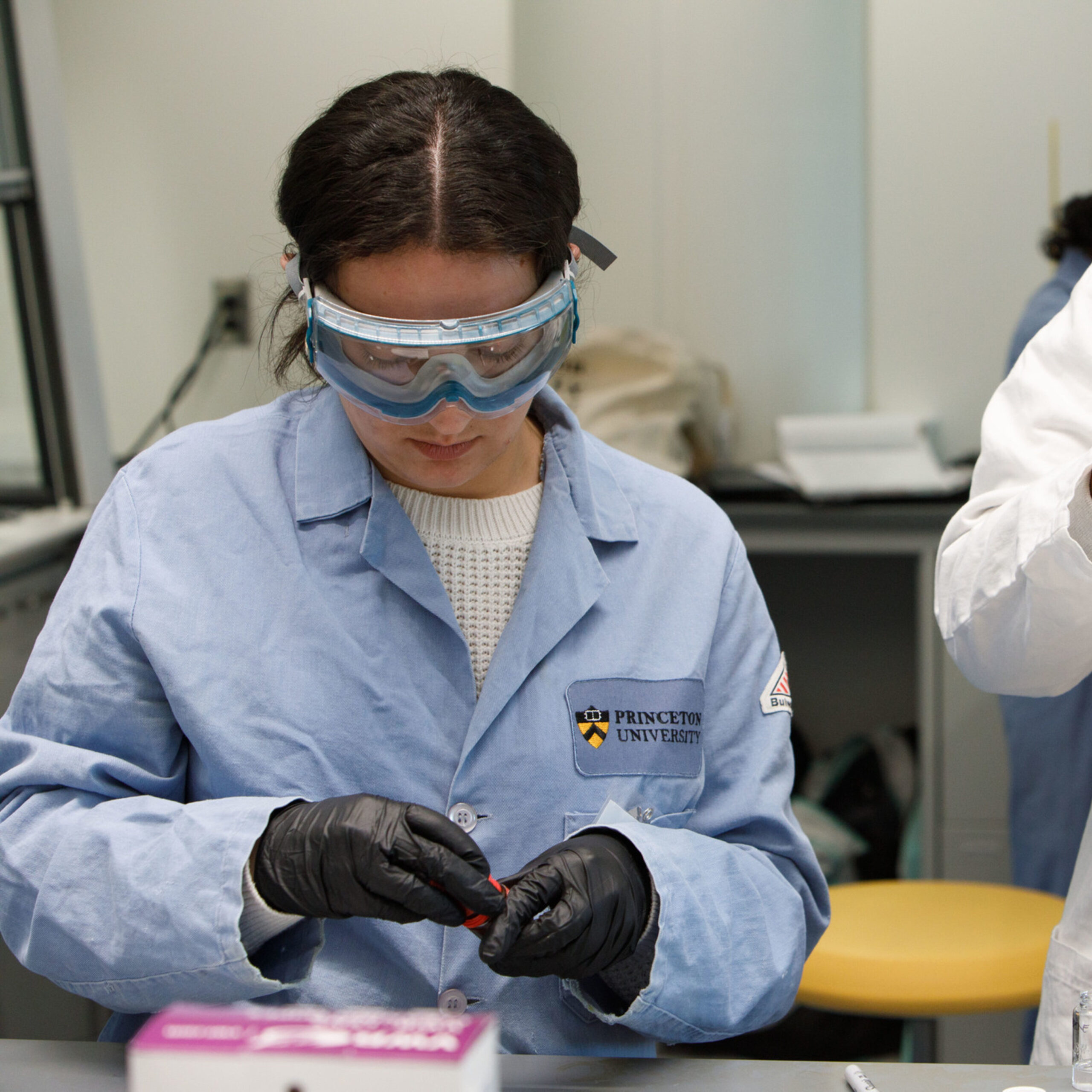 Two women students in lab coats performing a chemistry experiment.