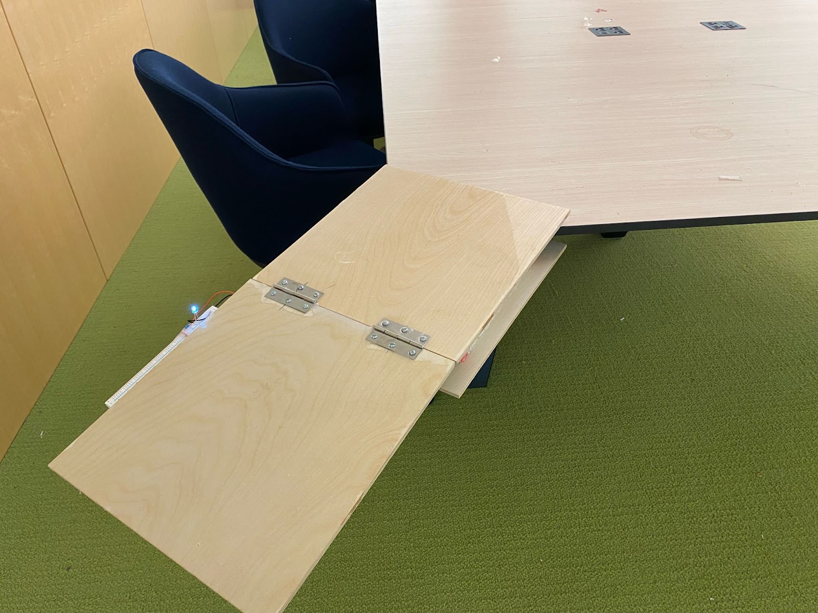 Desk Extender attached to light wood desk on green carpet near navy blue chairs.