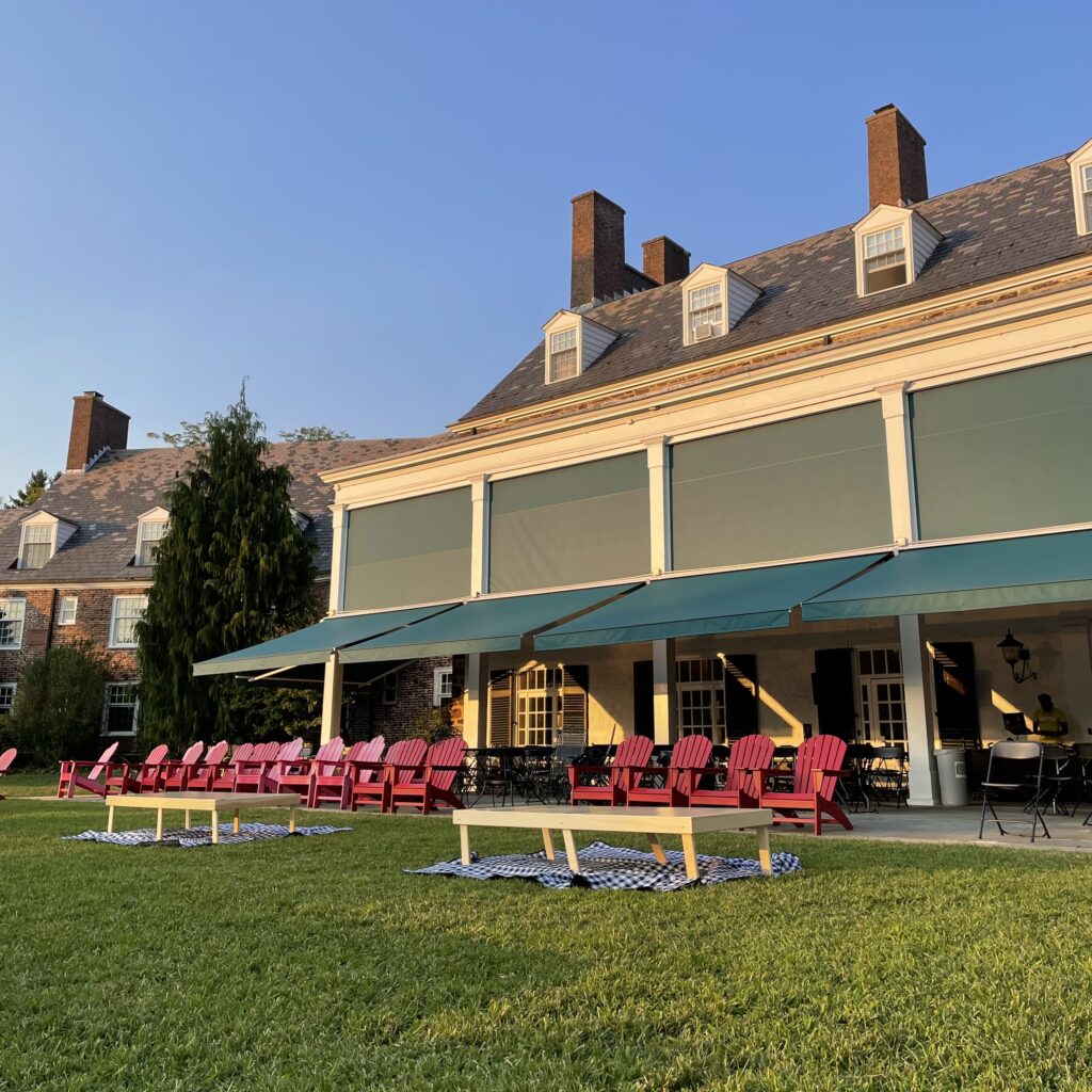 View of Forbes College with several red Adirondack chairs lined up and picnic tables and blankets on the lawn.