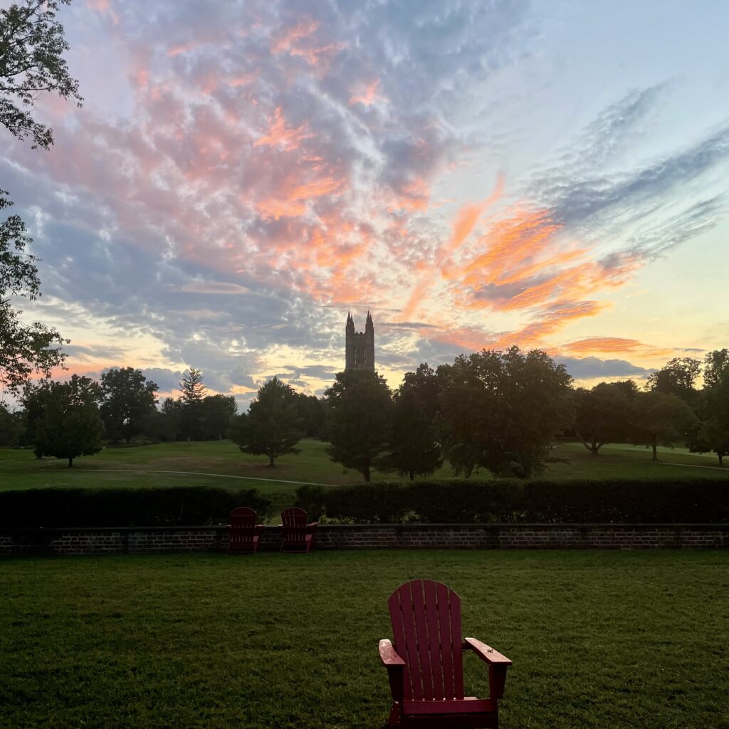Image of sunset over Princeton Graduate College, golf course, Forbes backyard. Red Adirondack chair in foreground.